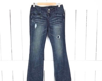May include: Dark blue denim jeans with a bootcut leg. The jeans have a high waist and a button fly. There are distressed details on the front of the jeans.