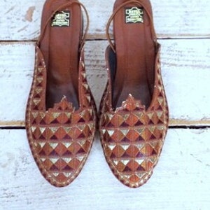 May include: A pair of brown leather shoes with gold geometric patterns. The shoes have a pointed toe and a low heel.