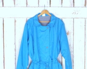 May include: A vintage, light blue jacket with long sleeves, a drawstring waist, and a button-up front. The jacket is hanging on a wooden hanger against a white wooden background. The jacket has a collar and a cinched waist.