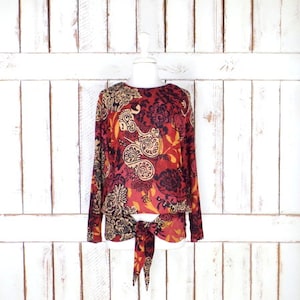 May include: A red, black, and gold long-sleeved blouse with a paisley print and a tie at the waist.