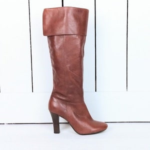 May include: Brown leather knee-high boots with a folded-over top and a high heel.