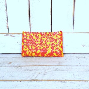 May include: A small, rectangular woven clutch purse with a yellow and red geometric pattern.