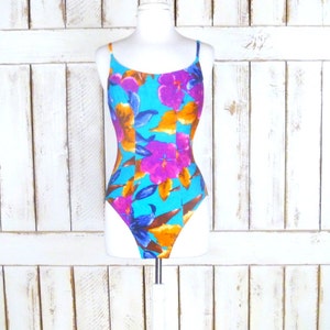 May include: A turquoise swimsuit with a floral print featuring pink, orange, and purple flowers. The swimsuit has thin straps and a scoop neck.
