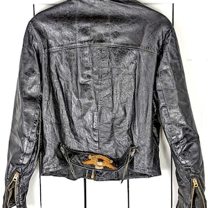 Puede incluir: Chaqueta de cuero negra para motocicleta con un logotipo de Harley-Davidson en la espalda. La chaqueta tiene una cremallera y dos bolsillos con cremallera en los lados.