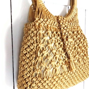 Op de afbeelding: Een beige gehaakte tote bag met een houten handvat. De tas heeft een geweven patroon en is gemaakt van natuurlijke vezels.