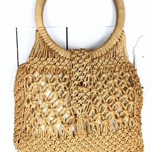 Op de afbeelding: Een beige gehaakte tote bag met een ronde houten handvat. De tas is gemaakt van geweven touwmateriaal.