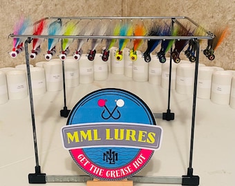 Può includere: Esposizione di esche da pesca colorate con varie combinazioni di piume e capelli. Le esche sono sospese da un supporto metallico, con un cartello che recita "MML LURES" e "GET THE GREASE HOT".