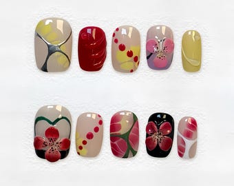 May include: A set of ten artificial nails with various designs. The nails feature colors like yellow, red, beige, and black, with floral and abstract patterns. Some nails have 3D flower embellishments.