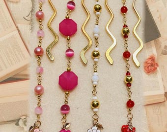 May include: Five decorative bookmarks with gold-colored wavy tops and beaded strands. The strands feature pink, white, and red beads, with flower charms at the bottom. The bookmarks are on a background of open books and aged paper.
