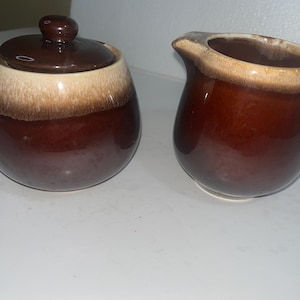 Puede incluir: Un juego de tres cuencos de cerámica anidados en tamaños graduados. Los cuencos presentan un acabado moteado y mate en tonos crema, marrón claro y marrón oscuro. El cuenco más grande tiene aproximadamente 18 cm de diámetro.