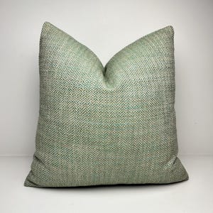 以下が含まれることがあります： 緑と白のヘリンボーン模様の正方形の装飾枕。枕は柔らかく、質感のある外観で、おそらく布製です。枕は明るい緑色で、リビングルームやベッドルームに適しています。