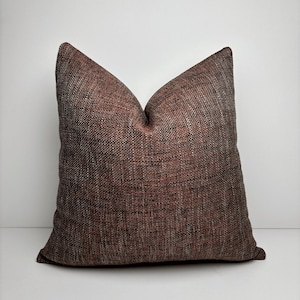 Könnte beinhalten: Ein quadratisches Zierkissen mit einem strukturierten, gewebten Stoff in Braun-, Rot- und Grautönen. Das Kissen hat eine klassische Form mit einer spitzen Oberseite, geeignet für ein Sofa oder Bett. Das Kissen hat eine neutrale Farbe und würde viele Einrichtungsstile ergänzen.