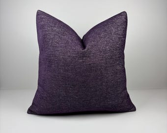 May include: A square decorative pillow in a deep purple hue. The pillow has a textured fabric, and the color is consistent across the entire surface. The pillow is placed against a white background.