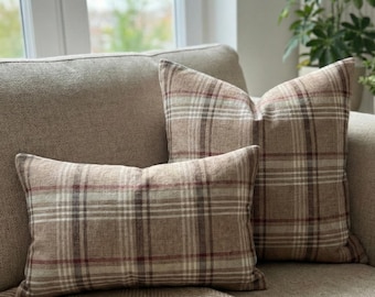 May include: Two decorative throw pillows with a plaid pattern in shades of brown, beige, and red. The pillows are rectangular and square, resting on a beige sofa. The pillows add a touch of warmth and texture to the living space.