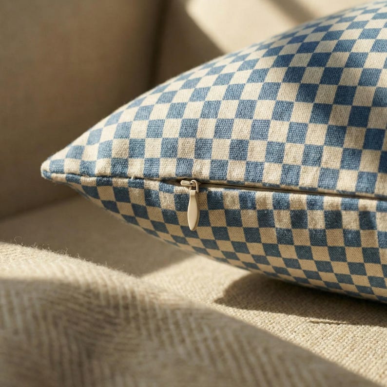 May include: A close-up shot of a cushion with a blue and beige chequered pattern. The cushion has a zip closure and is on a beige surface. The pattern is a repeating grid of blue and beige squares.