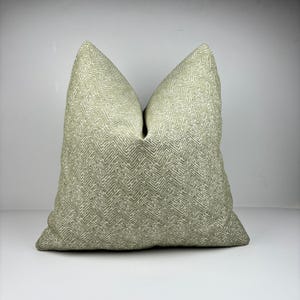 May include: A large, square decorative pillow in a light green color. The pillow features a repeating geometric pattern in a lighter shade of green. The pillow is made of a soft, textured fabric and is designed for home decor.