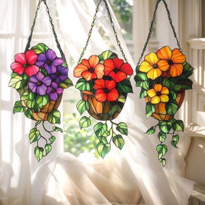 May include: Three hanging stained glass flower baskets. The baskets feature red, purple, orange, and yellow flowers with green leaves. Each basket is suspended by a chain, creating a decorative window display.