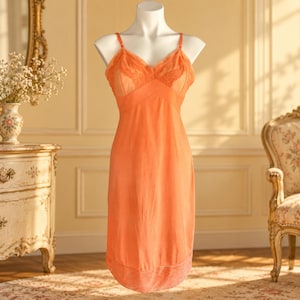 May include: A vibrant orange slip dress featuring a V-neckline with delicate lace detailing on the bodice, thin adjustable shoulder straps, and a matching lace trim along the bottom hemline, displayed on a white mannequin torso.