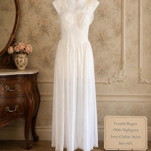 May include: An ivory floor-length nightgown made of chiffon and nylon, featuring a sweetheart neckline, ruffled shoulder straps, and a fitted bodice. A sign next to the garment reads: Formfit Rogers, 1960s Nightgown, Ivory Chiffon Nylon, Size 34 L.