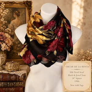 May include: A black silk scarf featuring a floral pattern in shades of deep red and golden yellow. The scarf displays the text OSCAR DE LA RENTA in red lettering. A tag indicates the scarf is 34 inches square and is new with tags attached.