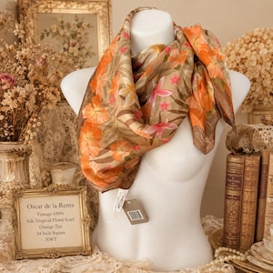 May include: A square silk scarf featuring a tropical floral pattern in shades of orange, tan, and brown. The scarf displays large hibiscus-like flowers and palm leaf motifs. A small white tag is attached, and it measures 34 inches square.