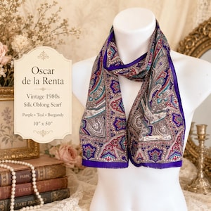 May include: An Oscar de la Renta vintage 1980s silk oblong scarf featuring a detailed paisley pattern in purple, teal, and burgundy. The scarf measures 10 inches by 50 inches and includes the designer's signature printed on the fabric.