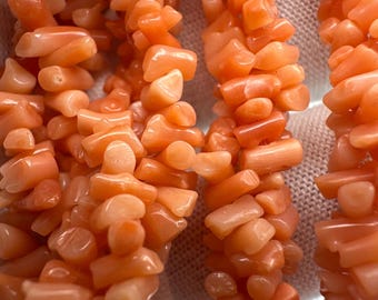 May include: Close-up of several strands of coral-colored gemstone beads. The beads are irregularly shaped and appear to be strung together. The color is a warm, peachy orange. The beads are likely used for jewelry making.