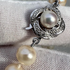 May include: Close-up of a pearl necklace clasp. The clasp is silver with a swirl design and small clear stones. The necklace features large, creamy-coloured pearls.