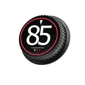 May include: Black lens cap with a red and white graphic. The graphic features the number "85" in white, a red ring, and the text "F 1.4" at the bottom. The cap has a ridged, textured edge.