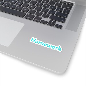 May include: A die-cut sticker featuring the word Homework in a bright cyan blue font with a white outline. The sticker is adhered to the silver metallic surface of a laptop computer, positioned below the keyboard and above the trackpad area.