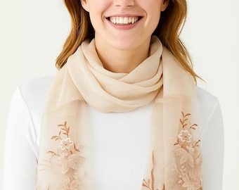 May include: A sheer, beige scarf with embroidered floral details. The scarf is draped around the neck and shoulders, with the floral embroidery in shades of brown and beige. The background is a plain white.