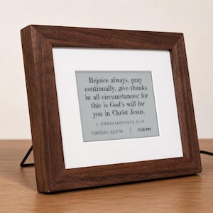 May include: A digital display frame with a dark brown wooden border and a white mat. The screen shows the text: Rejoice always, pray continually, give thanks in all circumstances; for this is God's will for you in Christ Jesus. 1 THESSALONIANS 5:16 TUESDAY, JULY 14 | 11:12 PM.