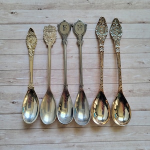 May include: A white ceramic mug with a black handle and the text "But First, Coffee" in a bold, black font. The mug is set against a blurred background, suggesting a cosy setting.