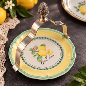 Könnte beinhalten: Ein runder Keramik-Servierteller mit gelbem Rand und grüner Umrandung, der in der Mitte eine Zitronenillustration und den Schriftzug Citrus limon zeigt. Der Teller verfügt über einen silberfarbenen Metallgriff mit einem dekorativen Knauf.