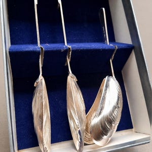 May include: Silver serving tongs and spoons, displayed in a blue velvet-lined box. The tongs have a curved handle and leaf-shaped ends. The spoons have a shell-like design. The box is white and silver.
