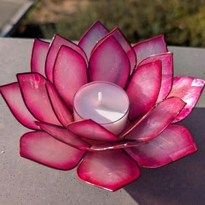 May include: A pink lotus flower-shaped candle holder with a white candle in the center. The petals are a vibrant pink with a pearlescent sheen. The candle is in a clear glass holder.
