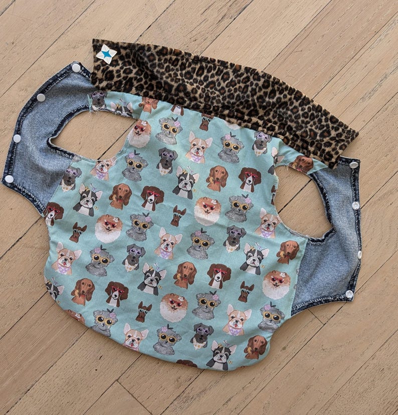 May include: A blue denim and leopard print dog car seat cover with a pattern of dogs wearing sunglasses on a light blue background.