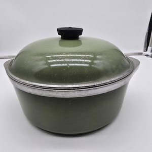 May include: A green enameled pot with a lid. The pot has a silver rim and handles. The lid is domed with a black knob. The pot is designed for cooking and is likely vintage.