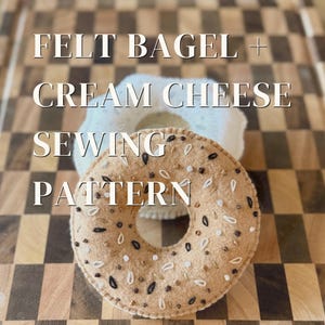 May include: A tan felt bagel with embroidered black, white, and brown seed details, positioned in front of a white felt cream cheese circle. The text FELT BAGEL + CREAM CHEESE SEWING PATTERN is overlaid on the image in white lettering.