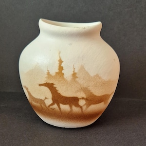 Peut inclure: Vase en céramique blanc cassé avec un motif de paysage marron. Le motif présente des silhouettes de chevaux en course, d'arbres et de montagnes. Le vase a une forme arrondie et une petite ouverture en haut.