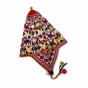 May include: A pointed knit hat featuring a vibrant, multi-colored geometric and animal-patterned design. The hat includes ear flaps, a small pom-pom at the top, and braided ties with additional pom-poms in shades of red, blue, pink, and cream.