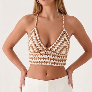 Puede incluir: Un top corto estilo halter con un patrón de cuadrados de ganchillo en tonos alternos de bronceado, marrón y blanco. La prenda tiene un escote en V profundo, tirantes finos trenzados que se atan detrás del cuello y un dobladillo recto.