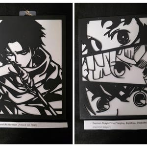 May include: Two black and white anime art pieces. One features Levi Ackerman from Attack on Titan, the other depicts the Demon Slayer Trio: Tanjiro, Zenitsu, and Inosuke. Each piece is a cut-out design with a white background.