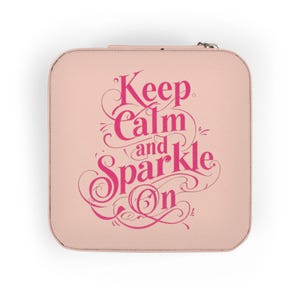 Könnte beinhalten: Ein quadratisches, hellrosa Schmucketui mit Reißverschluss. Auf dem Etui steht in dekorativer, pinkfarbener Schrift der Schriftzug "Keep Calm and Sparkle On". Das Etui ist geschlossen.