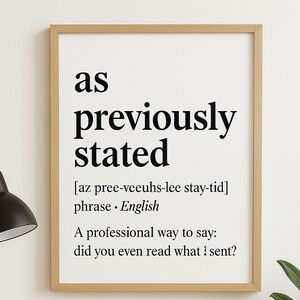 以下が含まれることがあります： 「as previously stated」というフレーズが黒い文字で書かれた額入りのプリント。ノートパソコン、ペン、ノート、鉢植えの植物が置かれた机の上にあります。黒いデスクランプも写っています。
