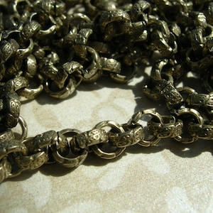 May include: A close-up of a silver chain with intricate designs on each link. The chain is made of metal and has a shiny finish.