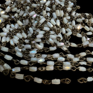 May include: A pile of white iridescent glass beads strung on a brass chain. The beads are faceted and have a subtle rainbow sheen.