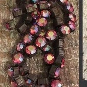 May include: A strand of iridescent purple and pink crystal beads with a silver metal backing. The beads are strung on a black elastic cord.