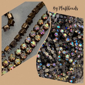 Puede incluir: Primer plano de dos hebras de cadena de strass iridiscente. La cadena está hecha de pequeños strass cuadrados que están engastados en un marco de metal. Los strass son una mezcla de colores, incluyendo oro, plata y negro. La cadena es perfecta para añadir un toque de brillo a cualquier proyecto.