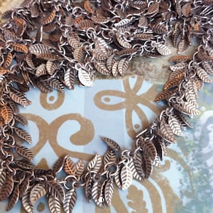 May include: A silver chain necklace with multiple silver leaf charms hanging from it. The necklace is on a patterned background.